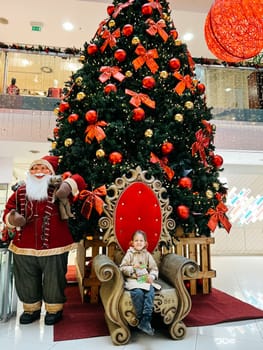 Little girl sits on an armchair near the Christmas tree in the mall. High quality photo