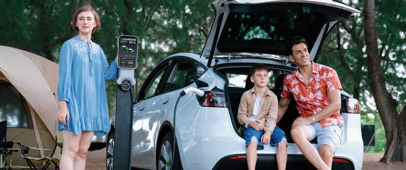 Outdoor adventure and family vacation camping in nature travel by eco friendly car for sustainable future. Lovely family recharge EV car with EV charging station in campsite. Perpetual