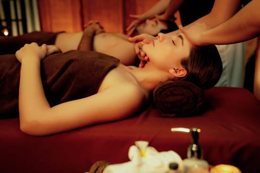 Couple customer enjoying relaxing anti-stress head massage and pampering facial beauty skin recreation leisure in warm candle lighting ambient salon spa in luxury resort or hotel. Quiescent