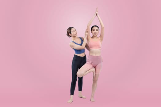 Asian woman in sportswear doing yoga exercise in standing pose with her trainer or yoga buddy. Healthy body care and meditation yoga lifestyle in full shot on isolated background. Vigorous