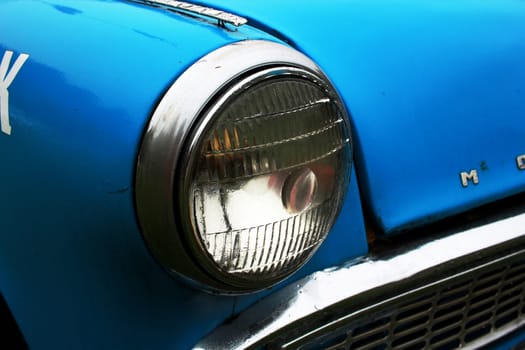 Photo of the front headlight of a blue old car. Transport. Retro. Vintage.