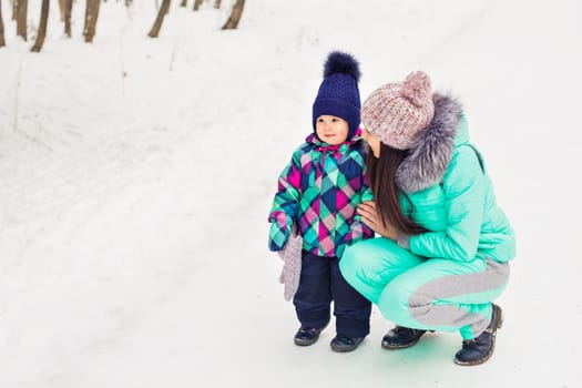 happy family mother and baby girl daughter playing and laughing in winter outdoors in the snow