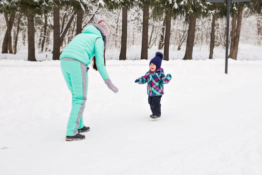 happy family mother and baby girl daughter playing and laughing in winter outdoors in the snow