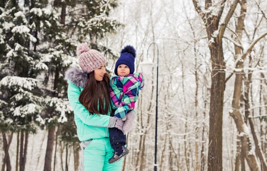 happy mother and baby in winter park. family outdoors. cheerful mommy with her child.