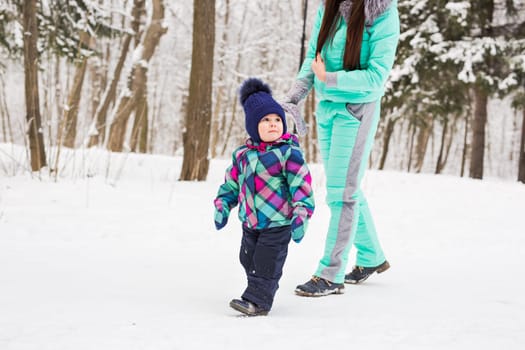 happy family mother and baby girl daughter playing and laughing in winter outdoors in the snow