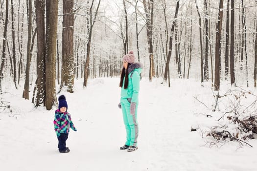 happy family mother and baby girl daughter playing and laughing in winter outdoors in the snow