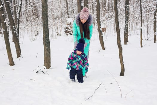 happy family mother and baby girl daughter playing and laughing in winter outdoors in the snow