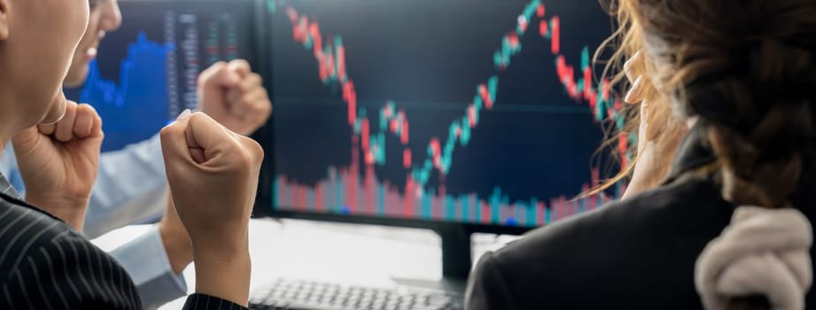 Happy successful business people celebrate while look at increasing stock market chart on black background displayed on computer. Smart investor cheering their success investment. Burgeoning.