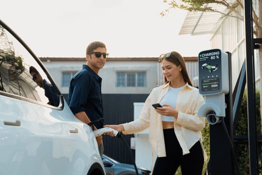 Eco-friendly conscious family couple recharging EV vehicle from home charging station. EV electric car technology utilized as alternative transportation for future sustainability. Expedient