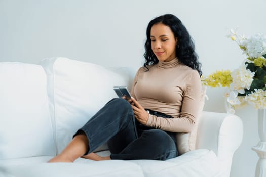 Relaxed young African American woman using crucial mobile phone on sofa couch in living room at home