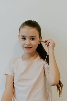 One beautiful Caucasian brunette girl with collected hair and in a pink T-shirt treats her ear with an infrared light device, standing against a white wall, close-up side view.