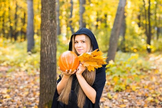 Halloween Witch with a magic Pumpkin in a dark forest. Beautiful young woman in witches hat and costume holding carved pumpkin. Halloween art design