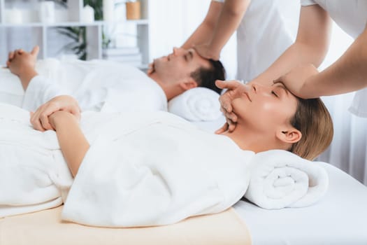 Caucasian couple enjoying relaxing anti-stress head massage and pampering facial beauty skin recreation leisure in dayspa modern light ambient at luxury resort or hotel spa salon. Quiescent