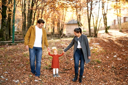 Mom and dad look at a little girl holding her hands while standing in the autumn forest. High quality photo