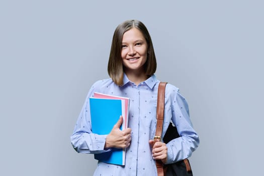 Portrait of young university student with backpack of textbooks on gray studio background. Smiling confident positive 20s female looking at camera. Education, knowledge, lifestyle, youth concept
