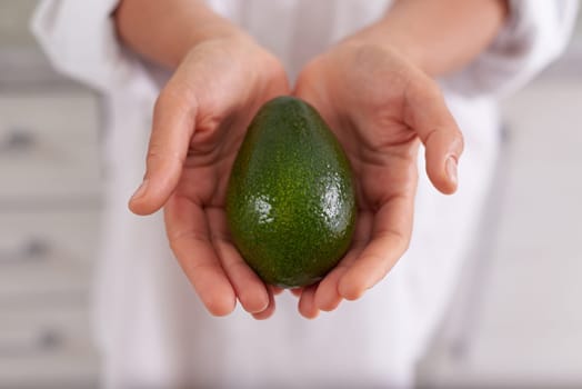 Closeup woman hands holding out at camera a fresh ripe organic avocado fruit. Selective focus. Healthy eating, vegetarianism, raw vegan diet and slimming concept. Sustainable lifestyle. Organic food