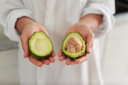 Closeup woman hands holding out at camera two halves of ripe organic avocado fruit. Selective focus. Healthy eating, vegetarianism, raw vegan diet and slimming concept. Sustainable lifestyle. Food
