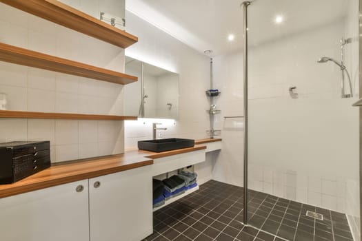 a bathroom with white tiles and wooden shelves on the wall, along with a glass shower stall in the corner