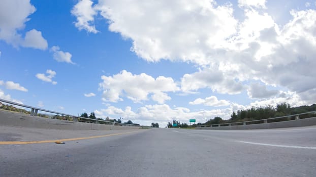 On a clear winter day, a car smoothly travels along Highway 101 near Santa Maria, California, under a brilliant blue sky, surrounded by a blend of greenery and golden hues.