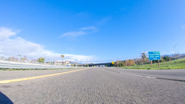 On a crisp winter day, a car cruises along the iconic Highway 1 near San Luis Obispo, California. The surrounding landscape is brownish and subdued, with rolling hills and patches of coastal vegetation flanking the winding road.