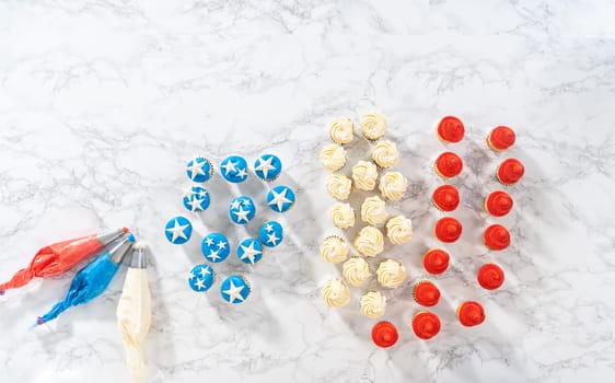 Flat lay. Frosting mini vanilla cupcakes with buttercream frosting to make an American flag mini cupcake cake.