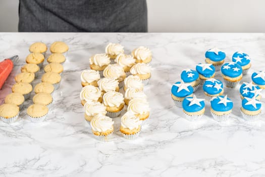 Frosting mini vanilla cupcakes with buttercream frosting to make an American flag mini cupcake cake.