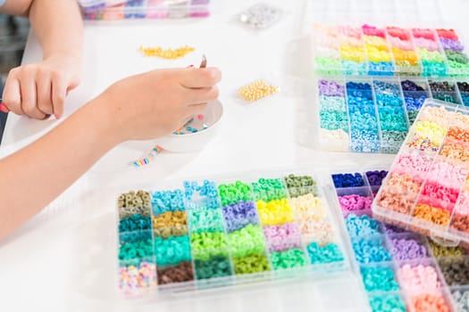 Little girl enjoys crafting colorful bracelets with vibrant clay beads set.