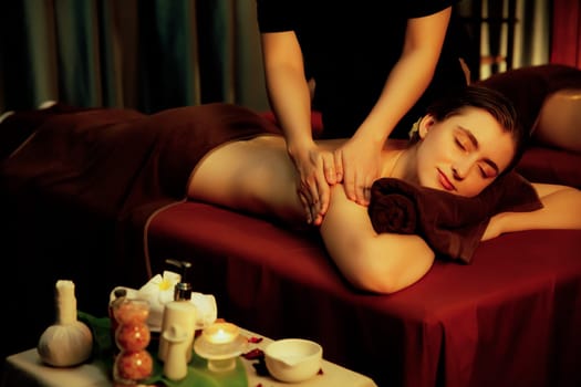 Caucasian couple customer enjoying relaxing anti-stress spa massage and pampering with beauty skin recreation leisure in warm candle lighting ambient salon spa at luxury resort or hotel. Quiescent