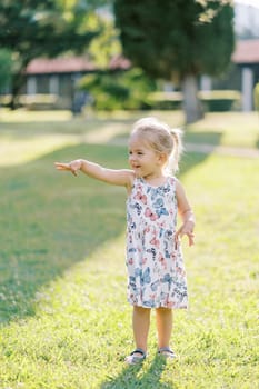 Little smiling girl stands in a sunny meadow and points forward with her hand. High quality photo