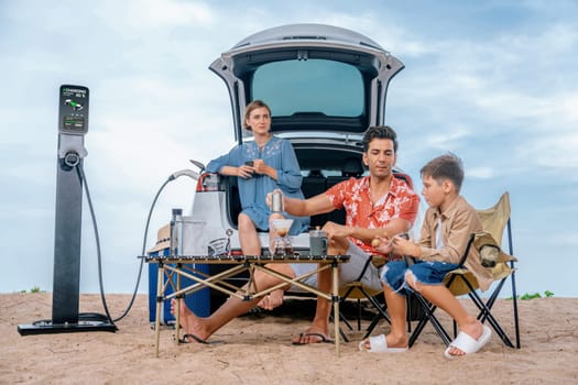 Family vacation trip traveling by the beach with electric car, happy family recharge EV car, enjoying outdoor camping coffee. Seascape travel and eco-friendly car for clean environment. Perpetual