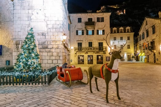 Christmas statue of a deer next to the red sleigh of Santa Claus near a sparkling Christmas tree. High quality photo