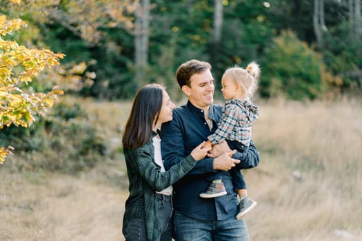 Mom hugs dad from behind with a little girl in his arms. High quality photo