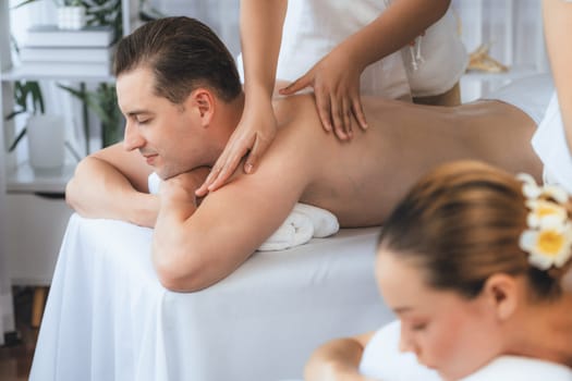 Caucasian couple customer enjoying relaxing anti-stress spa massage and pampering with beauty skin recreation leisure in day light ambient salon spa at luxury resort or hotel. Quiescent