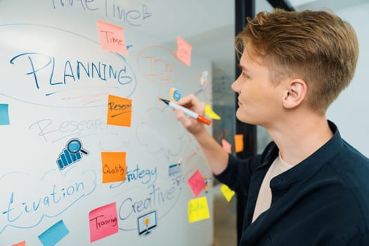 Professional caucasian male leader writing and sharing marketing idea by using mind map and sticky notes on glass board at modern meeting room. Creative business and planing concept. Immaculate.