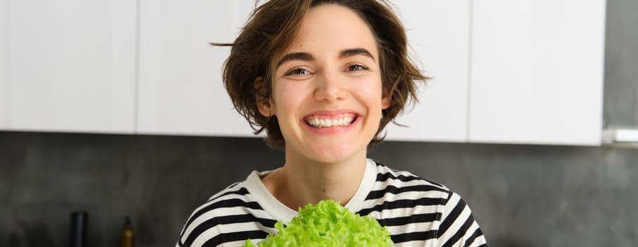 Close up portrait of beautiful, healthy smiling woman, posing with green lettuce leaf, cooking diet meal, preparing vegetarian salad, looking happy.