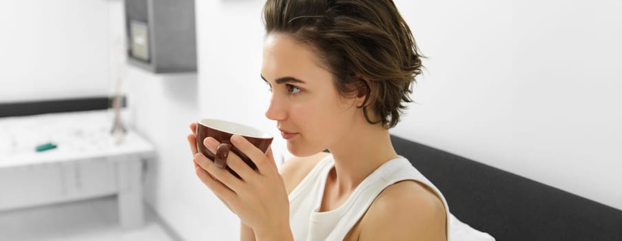 Portrait of woman smelling coffee, drinking morning cup in bed, waking up. Lifestyle concept