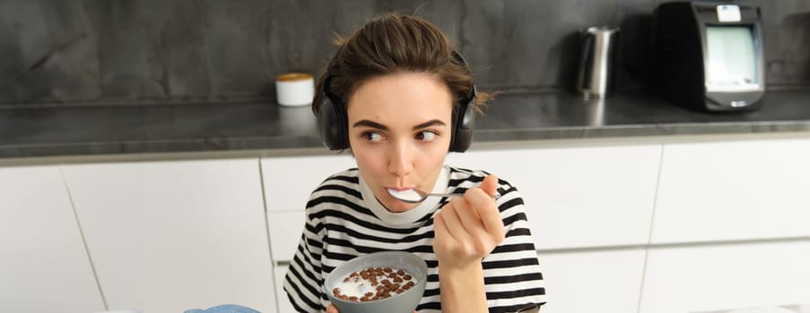 Portrait of carefree brunette woman, eating her cereals, listening to music, having breakfast in the kitchen.