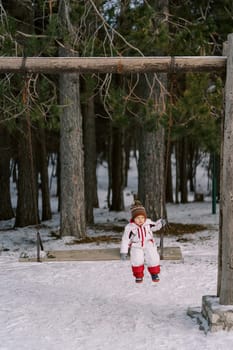 Little girl sits on a wooden chain swing in the forest. High quality photo