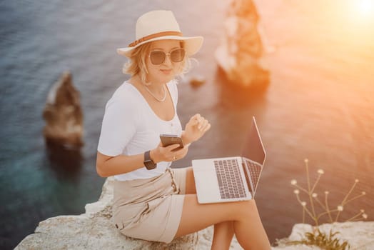 Freelance women sea working on the computer. Good looking middle aged woman typing on a laptop keyboard outdoors with a beautiful sea view. The concept of remote work