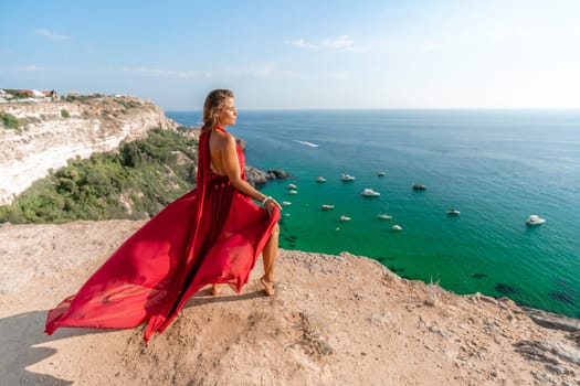 Woman sea red dress yachts. A beautiful woman in a red dress poses on a cliff overlooking the sea on a sunny day. Boats and yachts dot the background