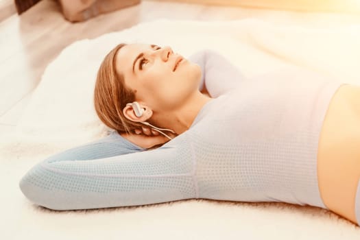 Top view portrait of relaxed woman listening to music with headphones lying on carpet at home. She is dressed in a blue tracksuit