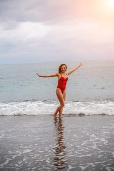 A beautiful and sexy brunette in a red swimsuit on a pebble beach, Running along the shore in the foam of the waves.