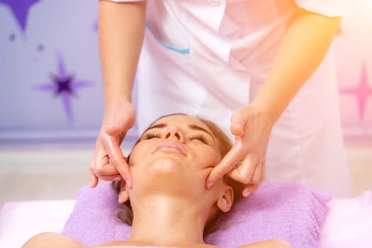 Relaxing massage. European woman getting facial massage in spa salon, side view.