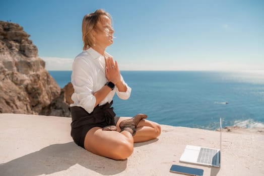 Freelance women sea working on the computer. Good looking middle aged woman typing on a laptop keyboard outdoors with a beautiful sea view. The concept of remote work