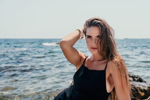 Woman travel sea. Young Happy woman in a long red dress posing on a beach near the sea on background of volcanic rocks, like in Iceland, sharing travel adventure journey