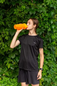 Fit tennage girl runner outdoors holding water bottle. Fitness woman taking a break after running workout.