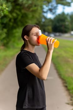 Fit tennage girl runner outdoors holding water bottle. Fitness woman taking a break after running workout.