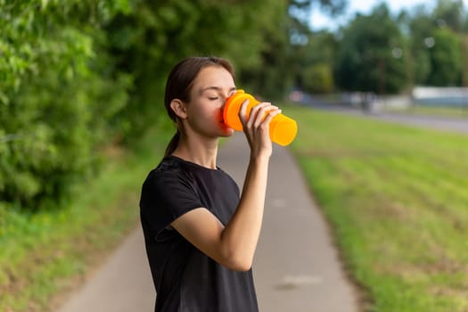 Fit tennage girl runner outdoors holding water bottle. Fitness woman taking a break after running workout.