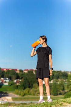 Fit tennage girl runner outdoors holding water bottle. Fitness woman taking a break after running workout.