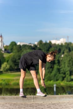 Young, fit and sporty girl in black clothes stretching after the workout in the urban city park. Fitness, sport, urban jogging and healthy lifestyle concept.